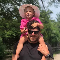 portrait of John Zanussi wearing sunglasses with his daughter on his shoulders