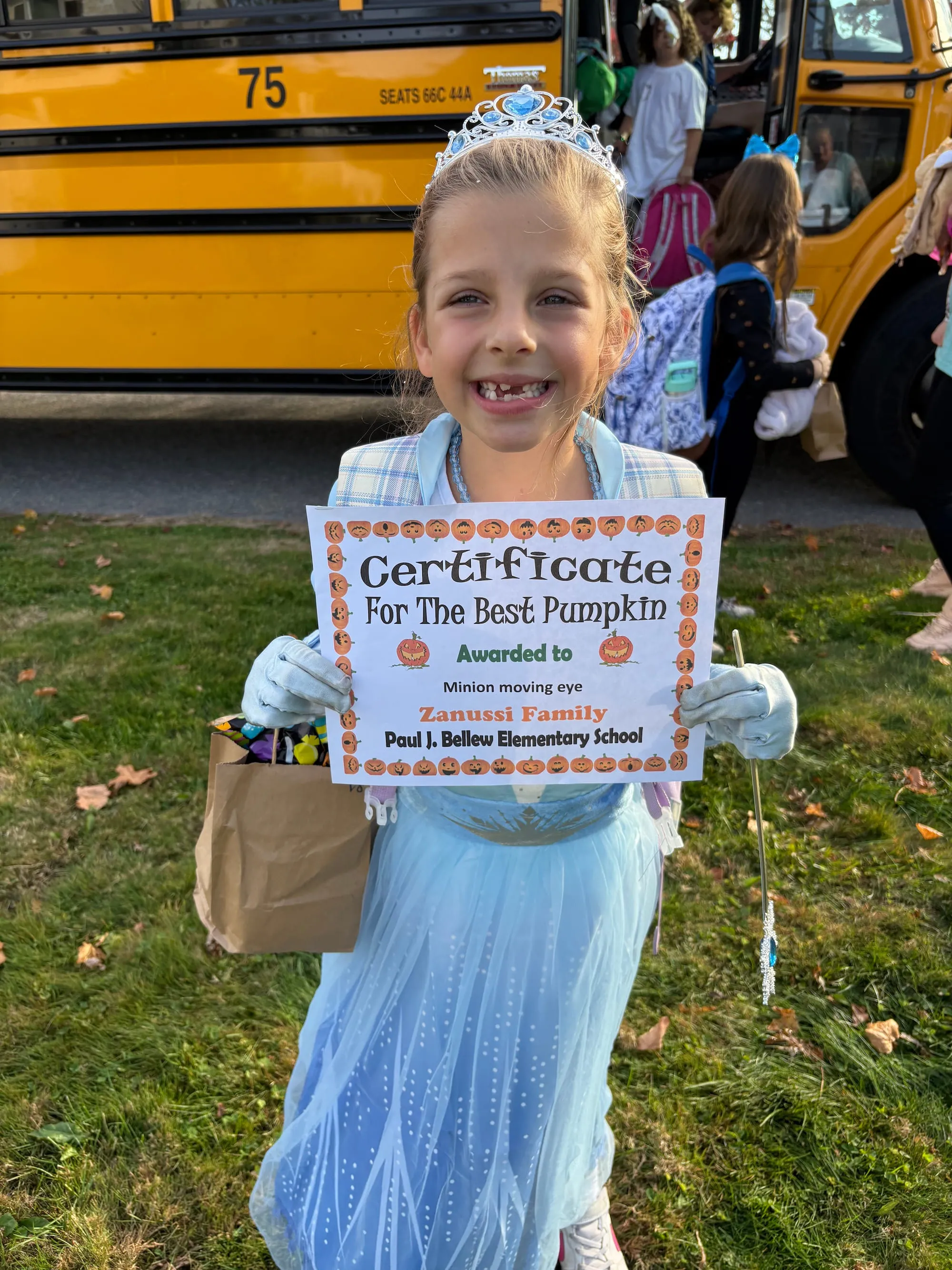 Natalia standing in front of her bus holding a paper that says "Certificate for the best pumpkin awarded to Zanussi Family"