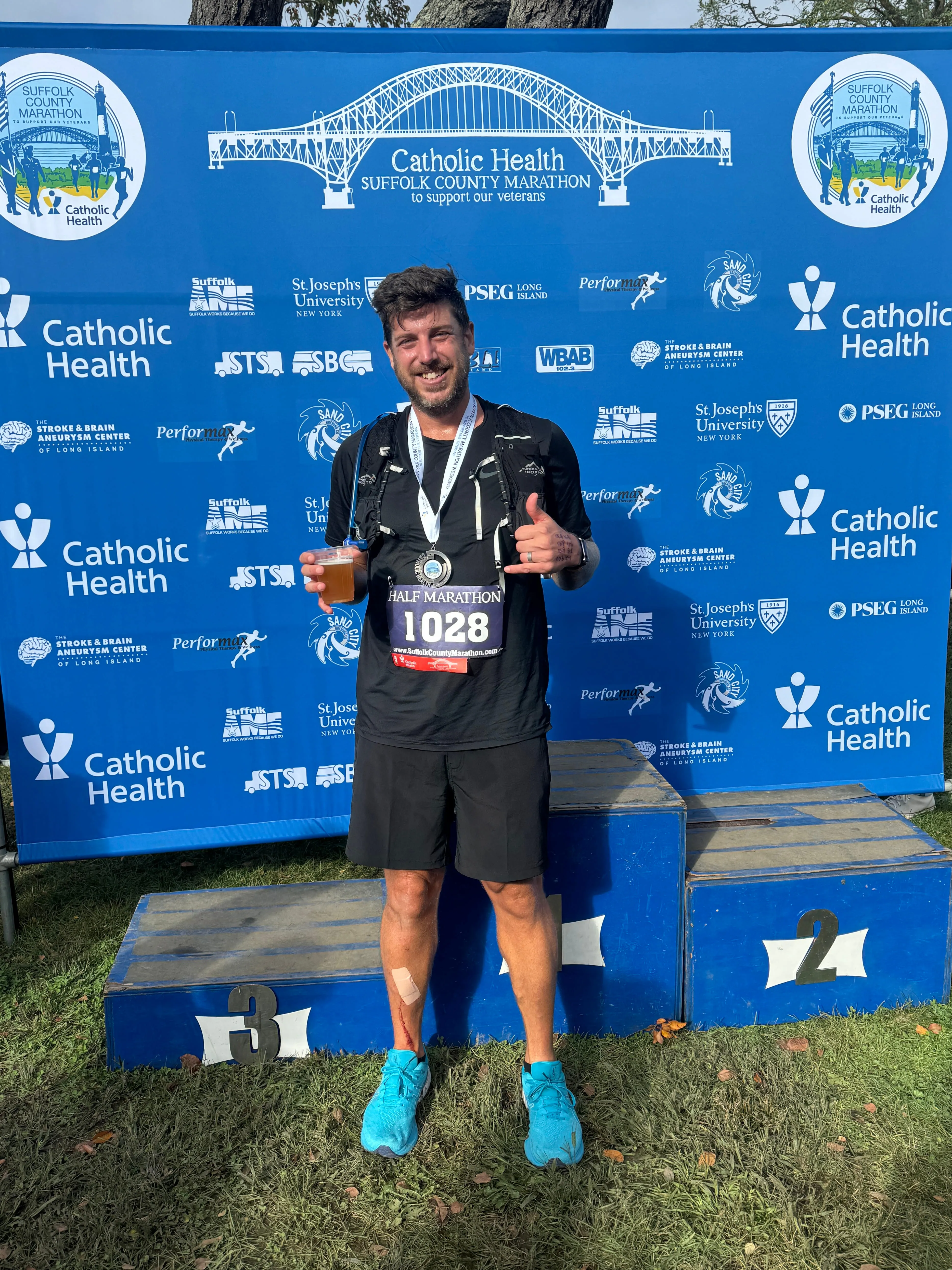 John standing in front of the podium holding a cup of beer after the race